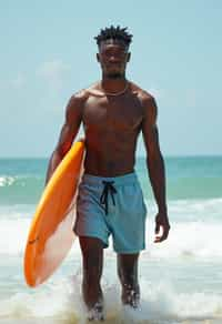 man in  board shorts with surfboard on the beach, ready to ride the waves