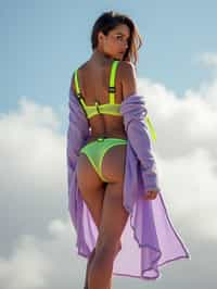 full body photo of full body photo of woman posing with her back to the camera, looking over her shoulder. she is wearing a highly stylized bikini lingerie consisting of lime green harness-like straps and a lavender glittery fabric draped over her shoulders. the background appears to be a cloudy, dreamlike sky, enhancing the surreal and artistic quality of the photograph. the lighting and composition focus attention on the contrast between her outfit and the soft background. she wears high heels. the photo emphasizes their exaggerated, idealized body shapes.