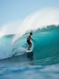 man as individual surfing a massive wave in a clear, blue ocean